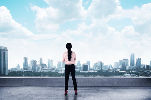 Asian business woman looking to the city from rooftop building