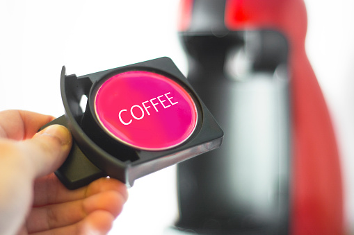 A coffee capsule and a coffee machine in the background