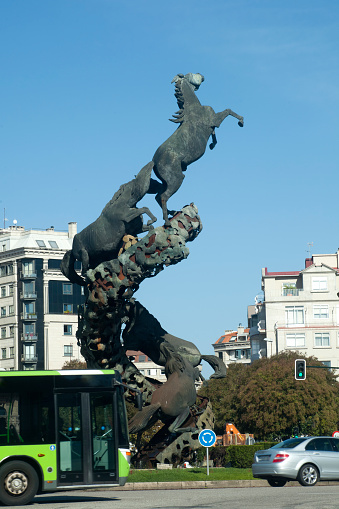 Vigo, Spain - October 8, 2015: Spain square in downtown Vigo, Pontevedra province, Galicia, Spain. Traffic on the runabout, horses sculpture and residential building in the background. Blue sky background.