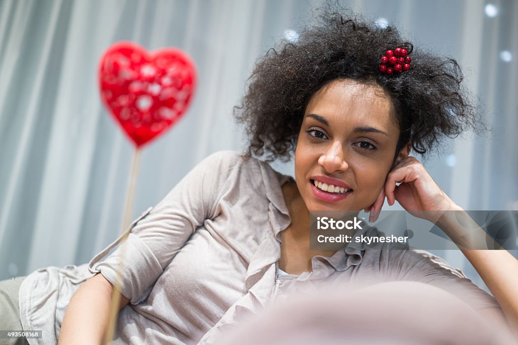Smiling African American woman enjoying at home. Young African American woman sitting on sofa at home and smiling while looking at the camera. 2015 Stock Photo