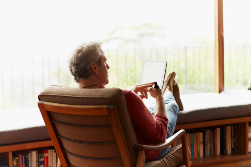 Rear view of mature man using digital tablet while relaxing on armchair at home