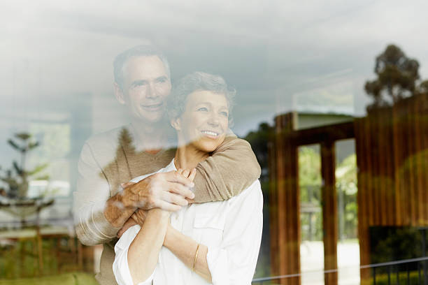 Thoughtful couple looking through window Thoughtful mature couple looking out through window at home two people thinking stock pictures, royalty-free photos & images