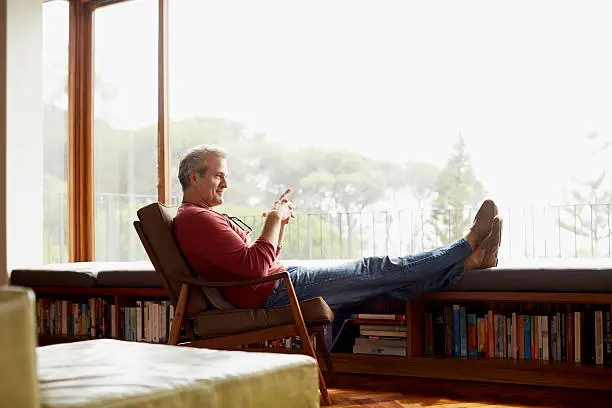 Full length side view of thoughtful mature man relaxing on armchair at home