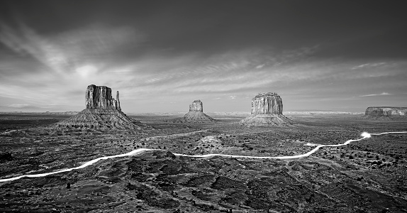 Black and white photo of the Monument Valley with car lights trails at night, USA.