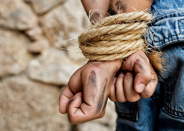 Prisoner bound with rope Dirty prisoner, arms bound behind back with rope, standing next to a stone wall. tangled photos stock pictures, royalty-free photos & images