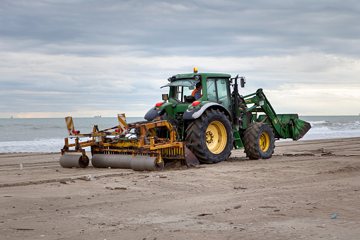 Marina di Ravenna, Italy - October 15, 2015: A middle-aged driver on a tractor doing beach maintenance after the end of summer season in Marina di Ravenna, Italy. Minor motion blur