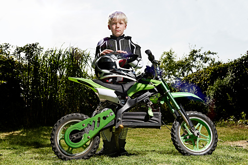 Young boy stands by its cross motorbike and looking straight into the camera