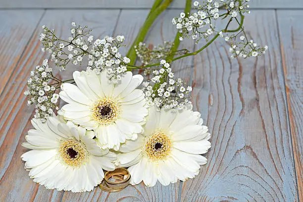 still life  with wedding rings and three white gerber daisies on old wooden shelves background with babies breath and empty copy space surface