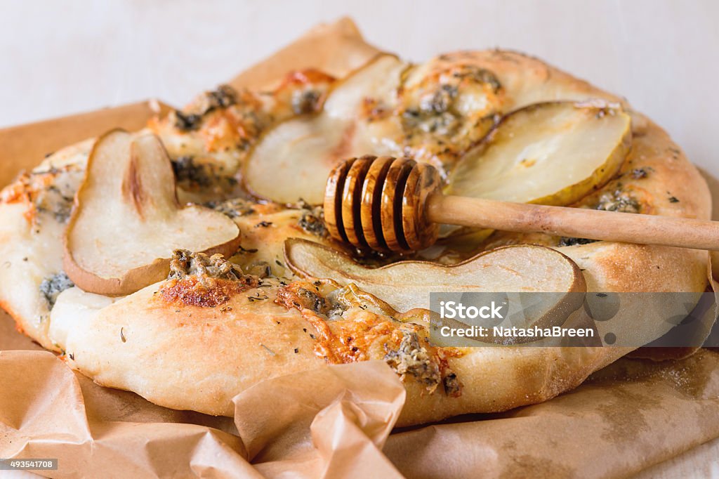 Pizza with pear and gorgonzola Whole Pizza with pear, gorgonzola and honey with olive wood honey dipper on baking paper over white wooden table. 2015 Stock Photo