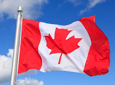 Canadian flag waving on the wind with blue sky and white clouds on the background, Quebec, Canada