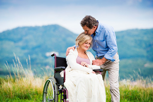 Senior man with woman in wheelchair outside in nature