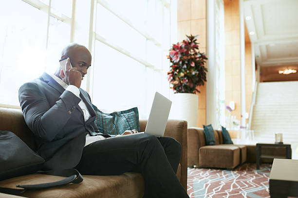 istock Businessman sitting in hotel lobby using cell phone and laptop 493550072