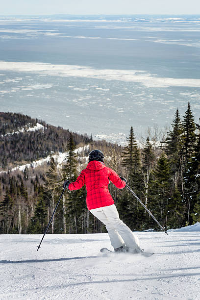 Woman Skier Going Down a Ski Slope DSLR picture of a woman skier going down a ski slope of Le Massif in Charlevoix, Quebec. The ski slope corduroy is visible and there is a river in the background. charlevoix photos stock pictures, royalty-free photos & images