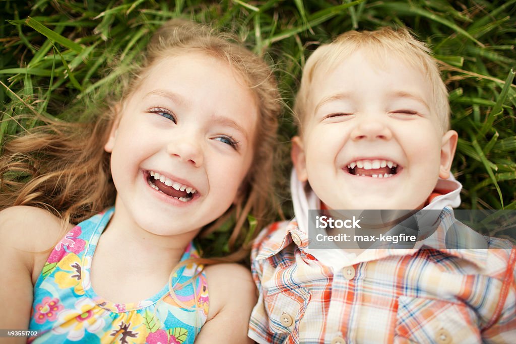 Sister and brother kids laughing. Top view. Top view portrait of two happy smiling kids lying on green grass. Cheerful brother and sister laughing together. Child Stock Photo