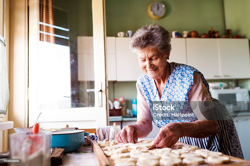 Senior woman baking Senior woman baking pies in her home kitchen. Cutting out circles from raw dough. 2015 Stock Photo