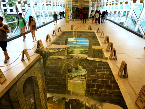 Bangkok, Thailand – May 11, 2014: 3D Street Painting Festival at the public skywalk near Ratchaprasong area, near the shopping mall area of Bangkok, Thailand. Passerby watches and walks past the art on the floor. Some try to play with the art.