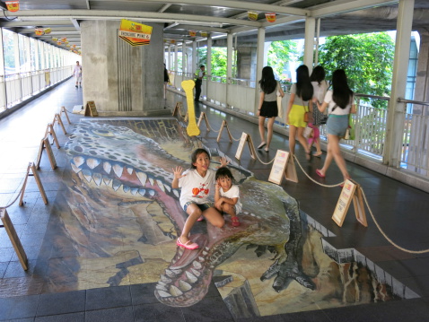 Bangkok, Thailand – May 11, 2014: 3D Street Painting Festival at the public skywalk near Ratchaprasong area, near the shopping mall area of Bangkok, Thailand. Passerby watches and walks past the art on the floor. Some try to play with the art.