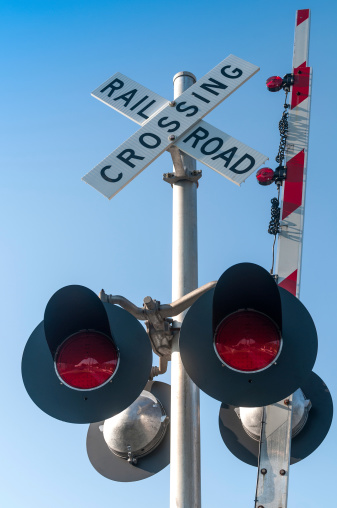 Railroad crossing sign and lights in front of a clear blue sky.
