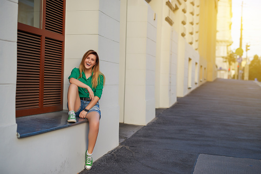 portrait of young woman enjoying her day, laughing and having fun outdoors, sitting near building.casual clothes.