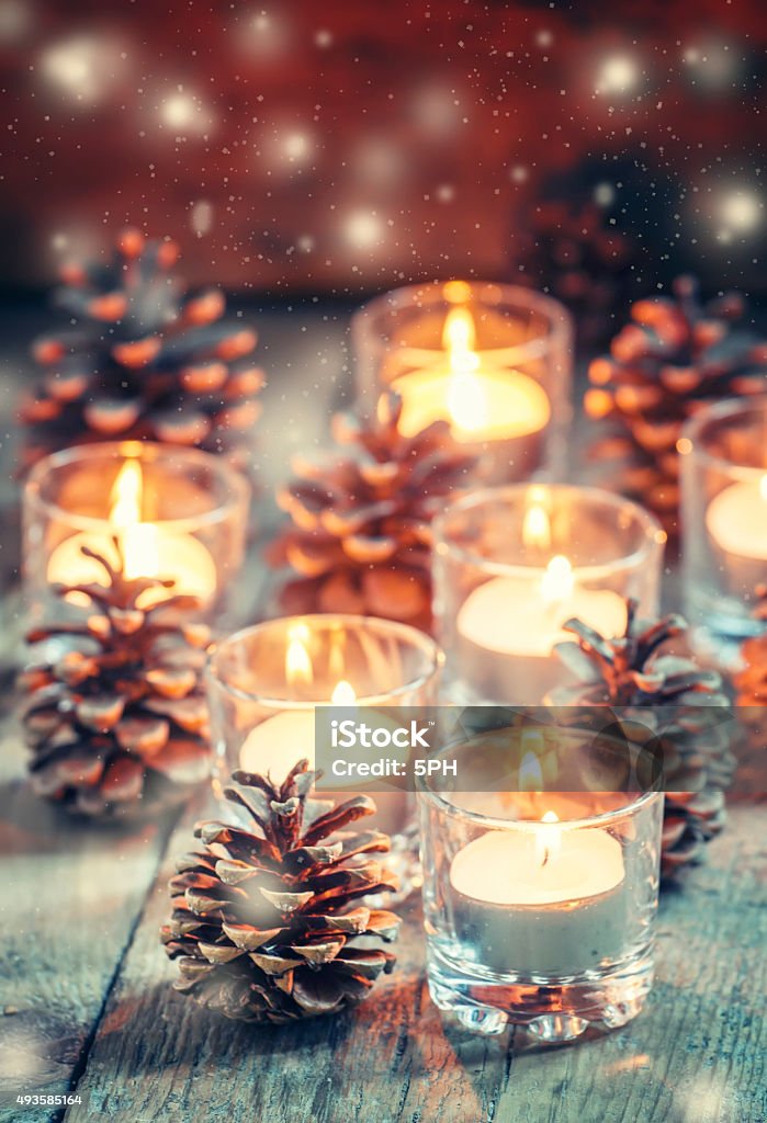 Christmas Christmas card with glowing small candle and fir cones Christmas Christmas card with glowing small candle and fir cones on old wooden background, dark toned image in country style, selective focus Christmas Stock Photo