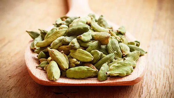 Green cardamom pods heap on wooden spoon rustic table background