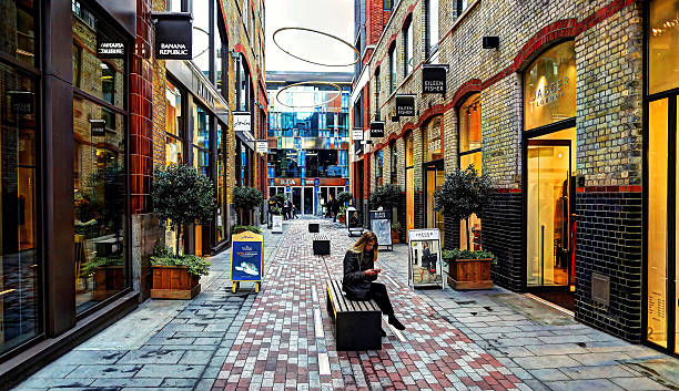 London, United Kingdom - October 28, 2012: Young woman sitting on a bench whilst checking her cell phone  outside shops in St Martin's Courtyard, Covent Garden.