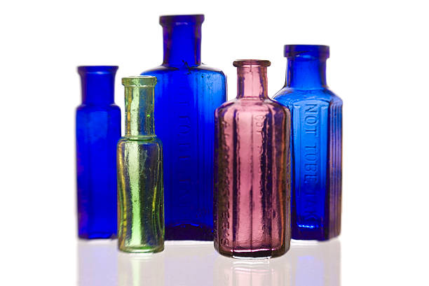 A close-up of antique pharmacy bottles on clear glass shelves. The amber and transparent bottles, paired with round white ceramic jars, present a vintage aesthetic. These neatly aligned containers evoke a sense of historical charm and represent bygone apothecaries. The photographed scene conveys cleanliness and order, suitable for themes involving nostalgia, history, and classical design.