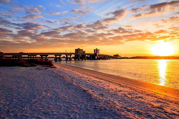 The sun rising over the land horizon with a long bridge and the ocean , nicely clouded ky bright colors in the sky Ft Myer Beach