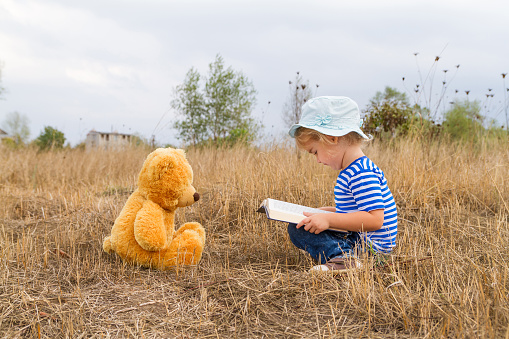 Cute girl reading book Teddy bear on the grass.