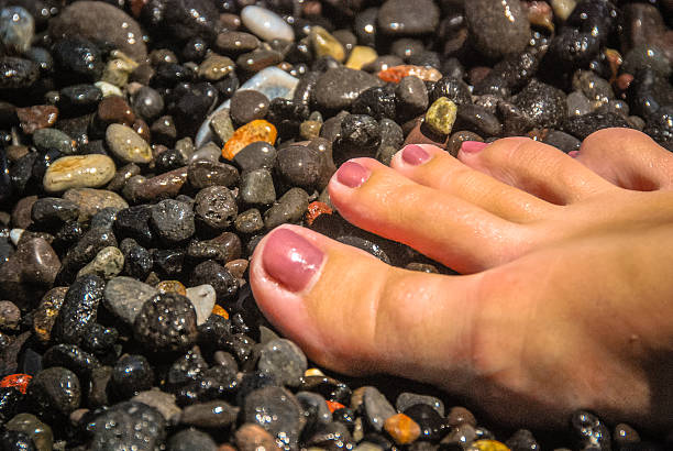 A young womans foot on a pebbly beach in Greece.
