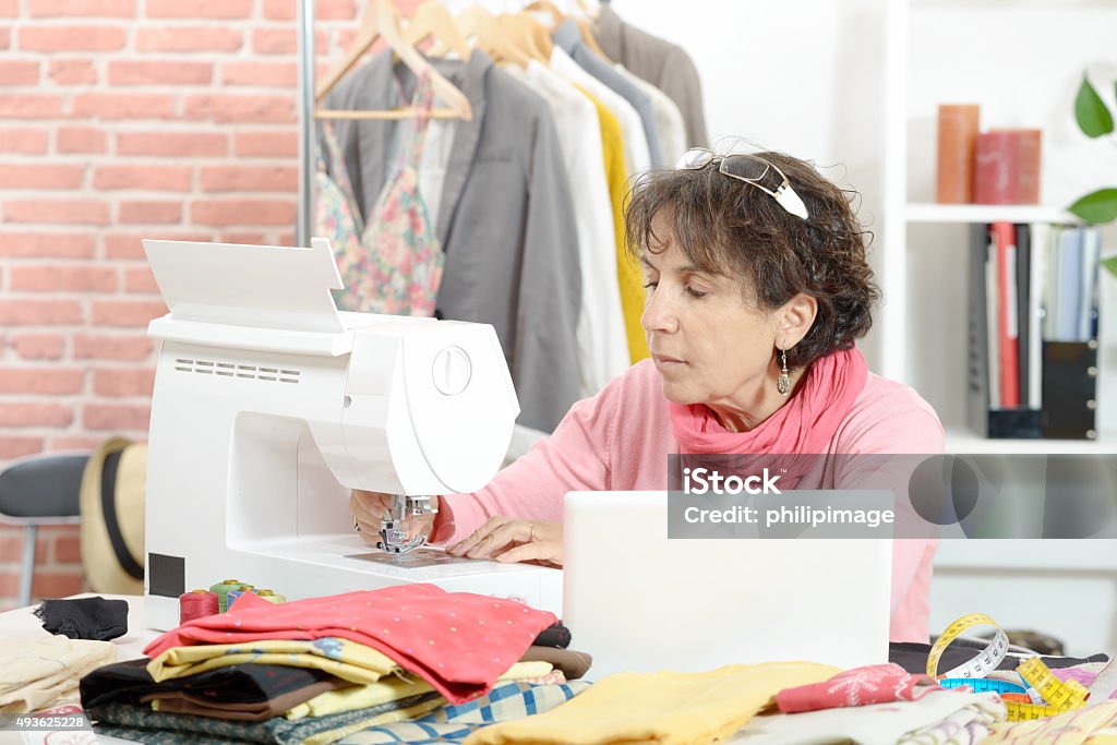 seamstress sitting at a sewing machine In a workshop, a seamstress sitting at a sewing machine 2015 Stock Photo