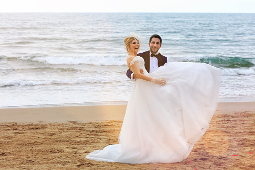 Groom carrying bride In arms at beach