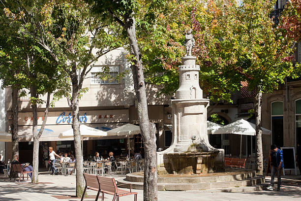 Vigo, Spain - October 8, 2015: Princesa square in old town Vigo, Pontevedra province, Galicia, Spain.   Fountain, plane trees, people in sidewalk cafes and residential buildings in the background. 