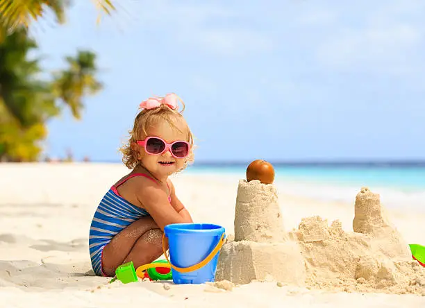 Photo of cute little girl playing with sand on beach