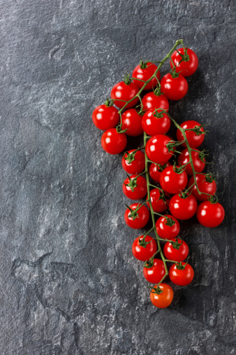 Cherry tomatoes on vine against black stone surface, composition with copy space