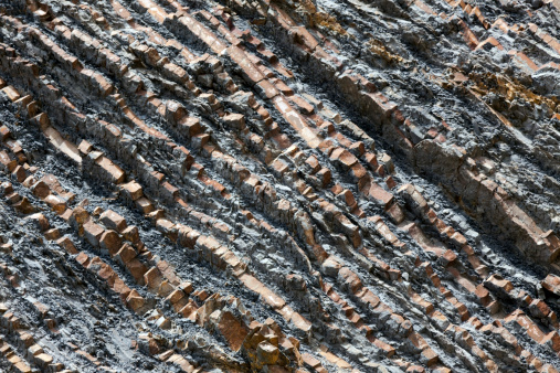 Close up view of a real and natural gray-color and steep rocky mountain slope, illuminated by the sunlight