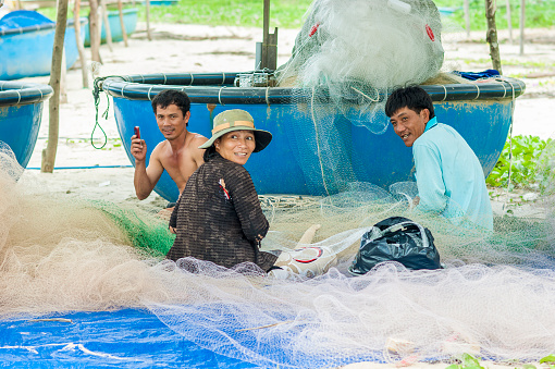 Binh Thuan, Vietnam - July 31, 2012: A fisher family mend the mesh of their fishing net together on the beach in Ham Tan District on Jul 31, 2012