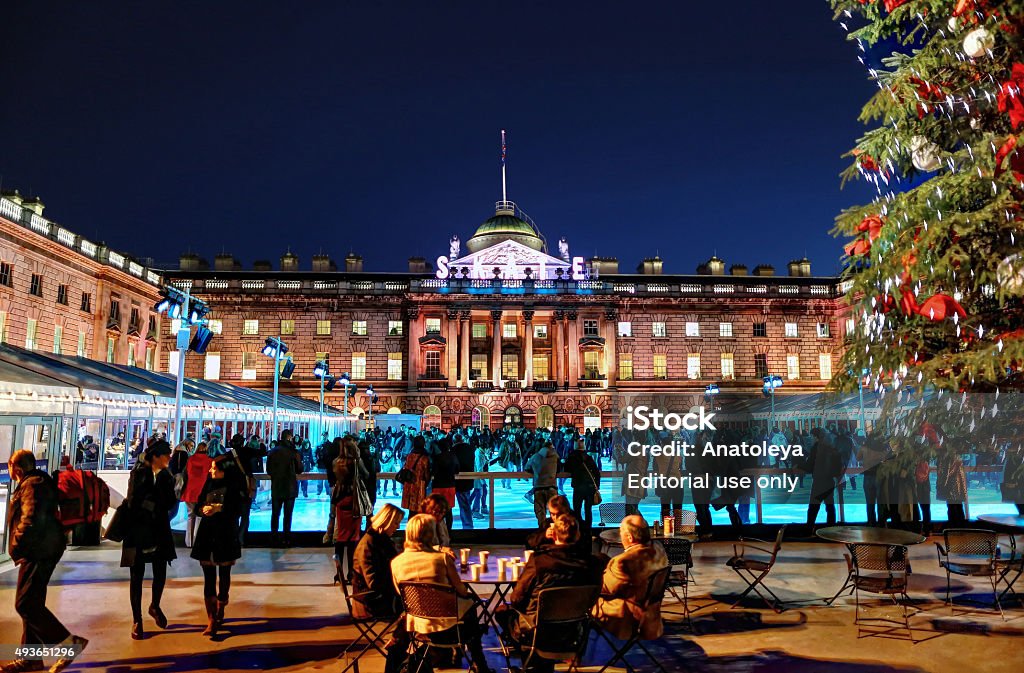 Ice Skating in Somerset House in the evening London, United Kingdom- November 22, 2012: Group of people sitting around a table next to a large Christmas tree in front of a crowded ice skating rink in Somerset House in the evening.  2015 Stock Photo