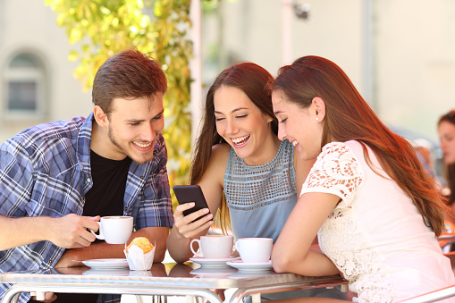 Three happy friends watching social media in a smart phone in a coffee shop