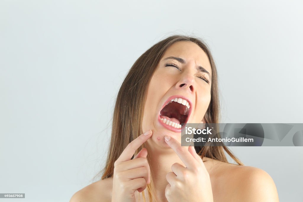 Girl crying while pressing a pimple on her chin Girl crying while pressing a pimple on her chin with a grey background Pimple Stock Photo