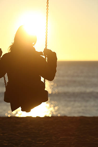 istock Woman silhouette swinging at sunset on the beach 493659040