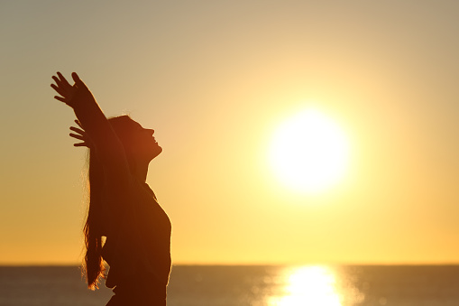 Woman breathing fresh air at sunset on the beach and raising arms