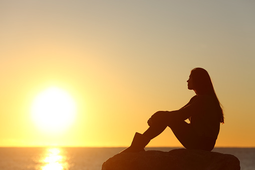 Woman silhouette watching sun in a sunset