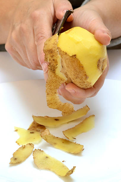Woman hands peels potato - macro on the white background