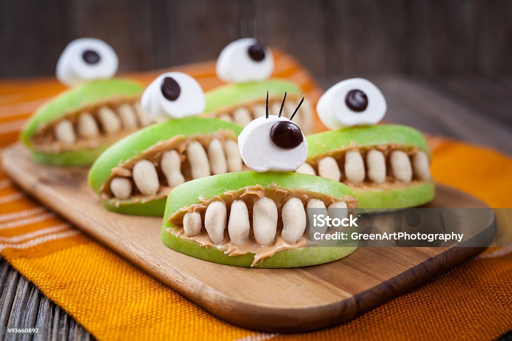 Spooky halloween edible apple monsters healthy natural dessert. Horror party Spooky halloween edible apple monsters healthy natural dessert. Horror party decoration delicious snack. Homemade cute cyclop mouth with teeth and peanut butter on dark vintage wooden table background. Halloween Stock Photo