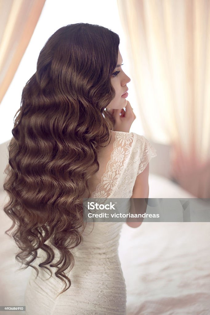 Beautiful brunette bride with long healthy wavy hair styling Beautiful brunette bride with long healthy wavy hair styling posing against the window in modern interior. Wedding Stock Photo