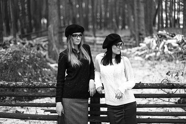 Portrait of young female friends leaning on tree and looking at camera in autumn park