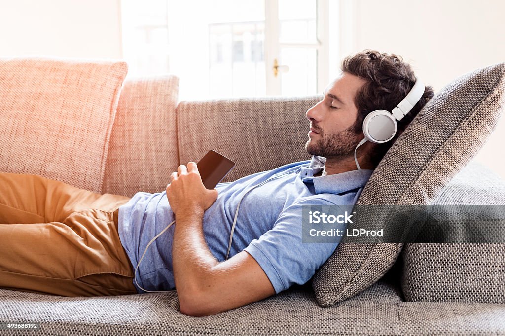 Hombre en el sofá para escuchar música con un smartphone - Foto de stock de Hombres libre de derechos