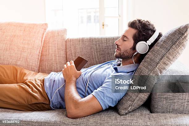 Hombre En El Sofá Para Escuchar Música Con Un Smartphone Foto de stock y más banco de imágenes de Hombres