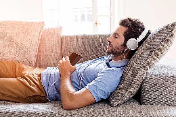 Man on his sofa listening to music with a smartphone stock photo